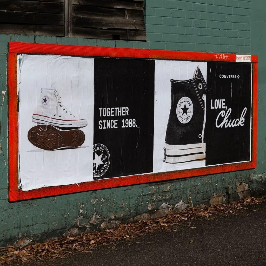 Outdoor Converse billboard featuring classic high-top All Star sneakers with the text “Together Since 1908. Love, Chuck.” displayed on a weathered wall.